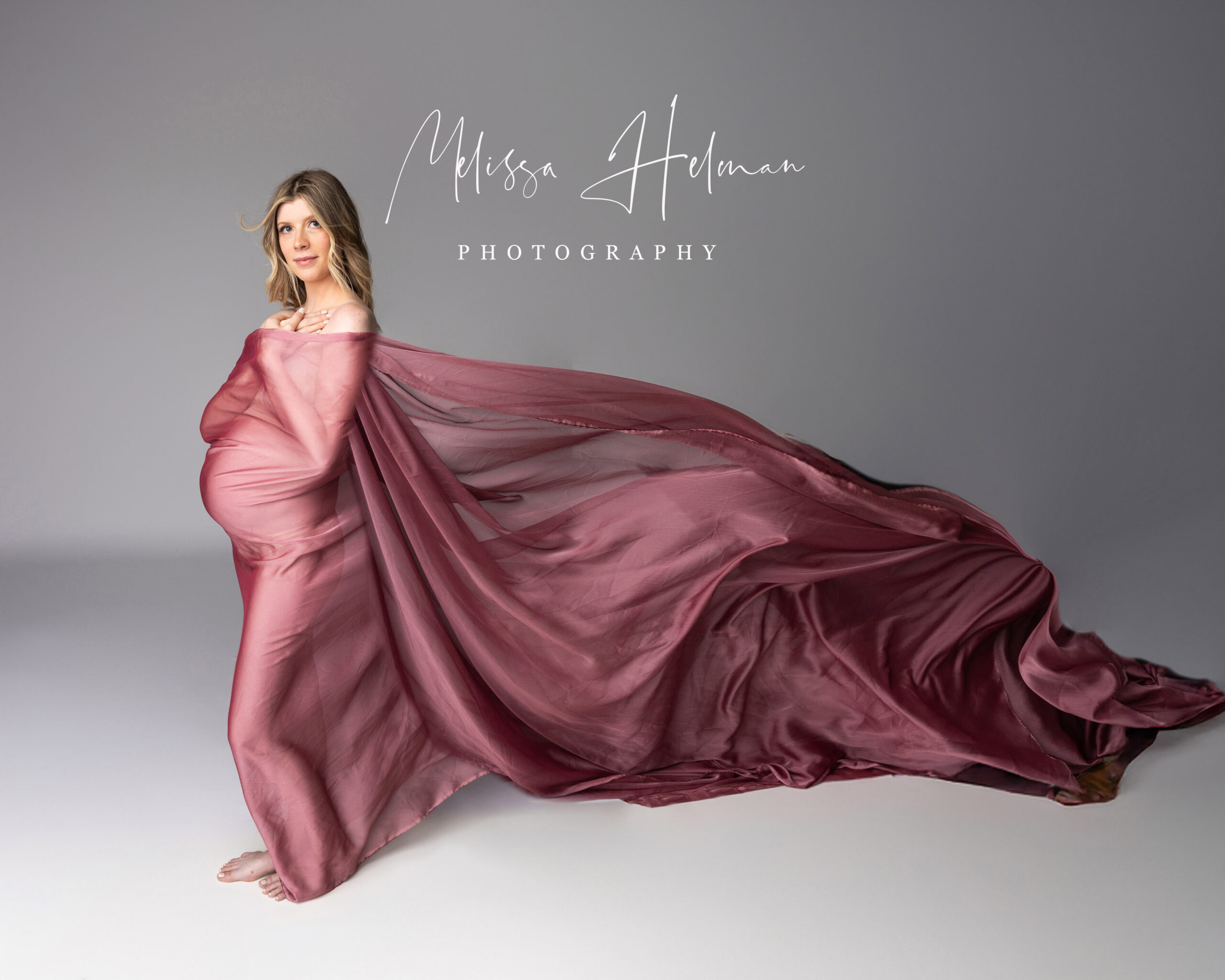 Pregnant mother standing with mauve fabric blowing in the wind.
