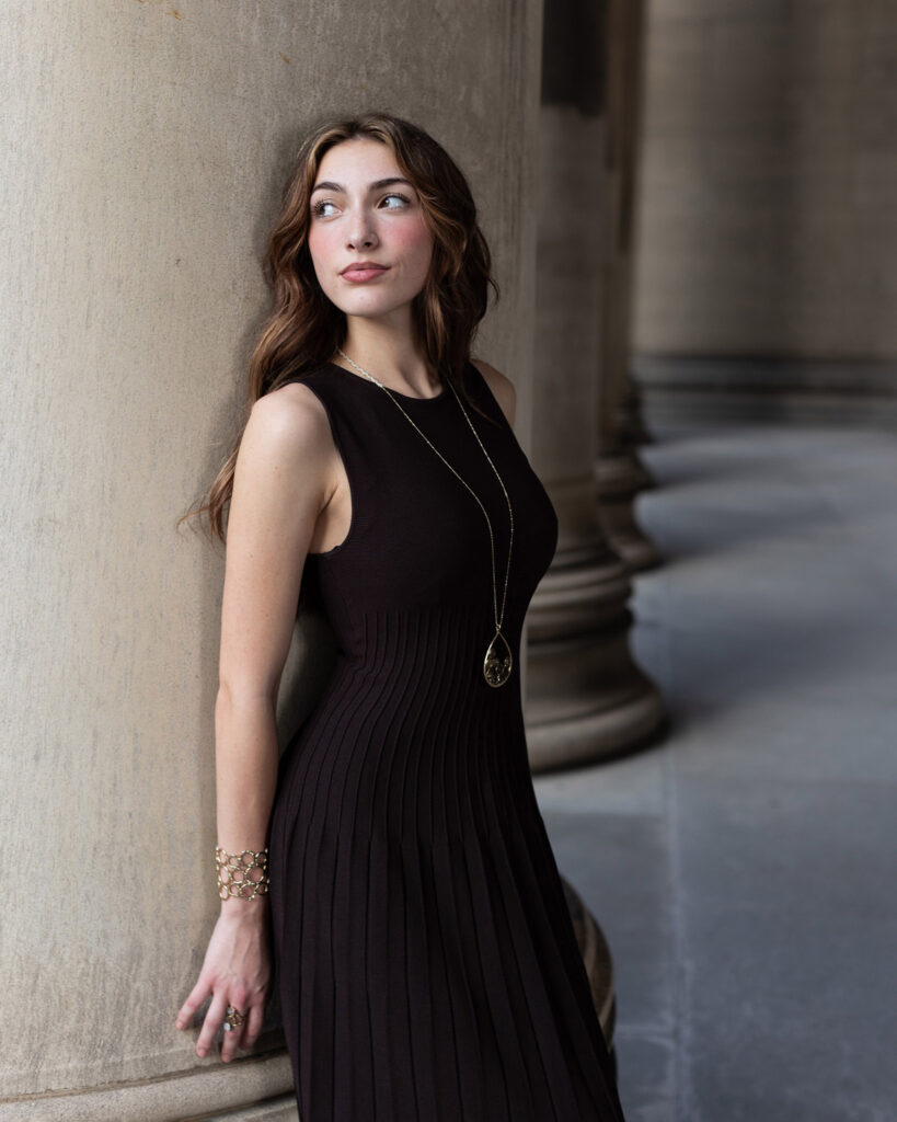 girl leaning on stone pillar in dress for senior photos looking away.