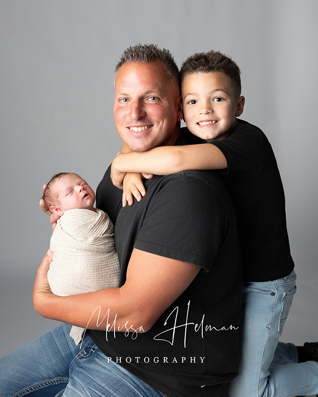 Dad holding newborn son with oldest son holding him around his neck