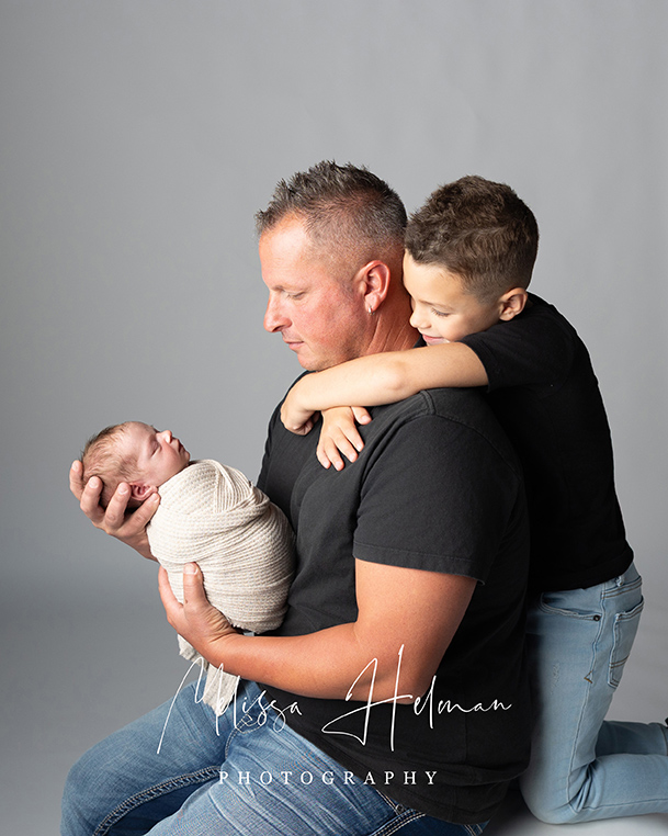 Dad holding newborn son with oldest son on his back