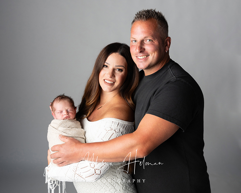 Mom and dad smiling at camera while holding their newborn son