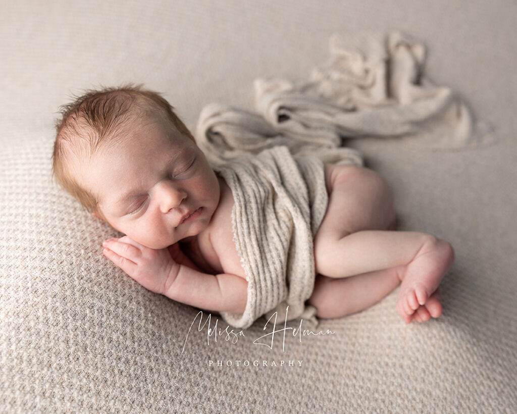 Newborn baby sleeping in neutral wrap during Pittsburgh studio photography session with legs curled up