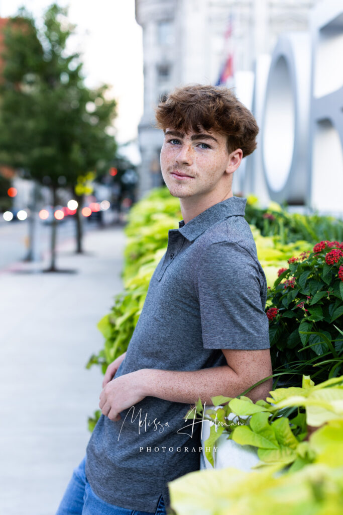 High school senior in casual outfit leaning against a textured wall downtown