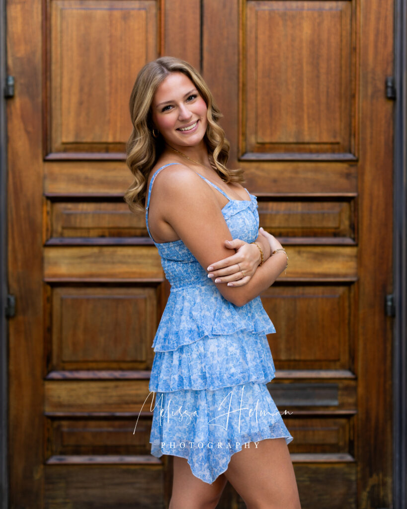 Close-up senior portrait with wood stained doors in blue dress 