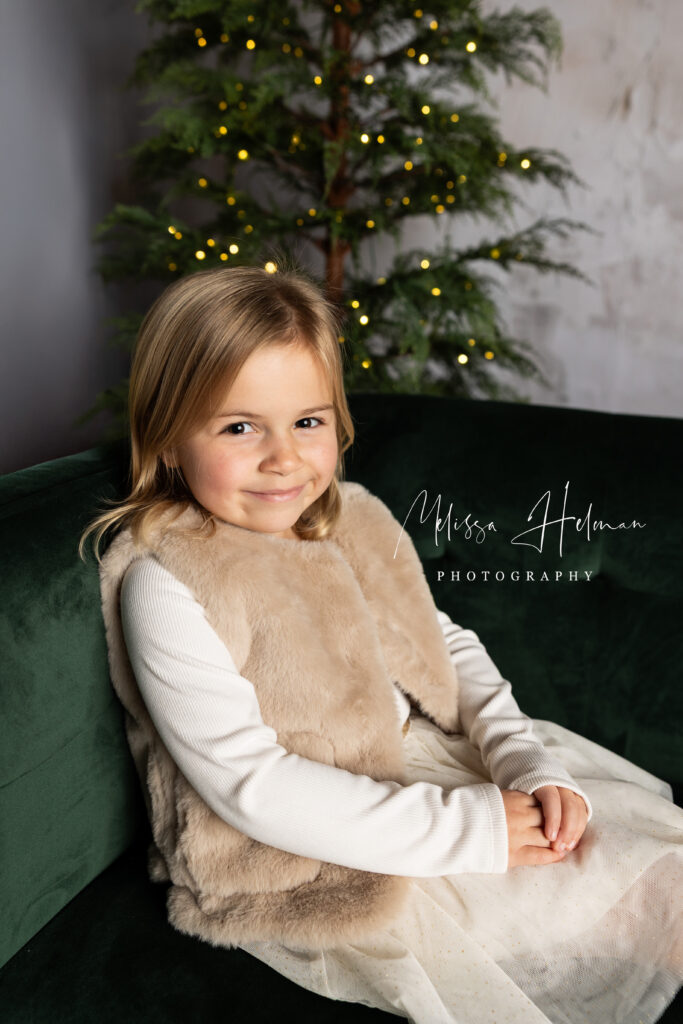 Girl sitting on green couch in fur vest for Holiday pictures.