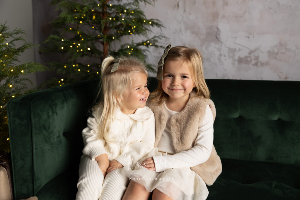 Sisters sitting together on a green velvet couch for their holiday pictures.