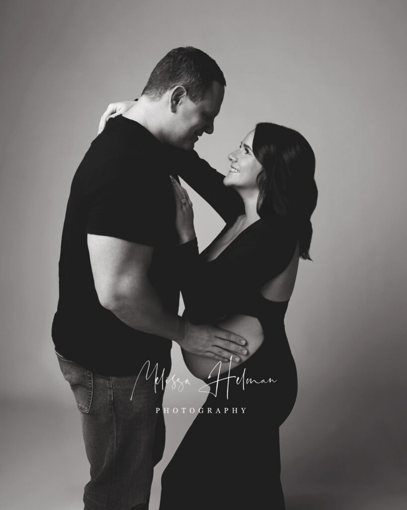 husband and wife pose together for maternity session in black and white